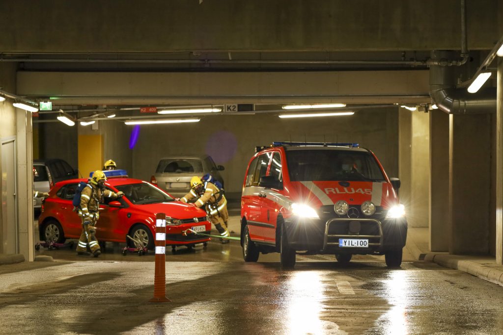 Ajoneuvoa siirretään parkkihallissa siten, että toinen auto hinaa, ja hinattavan auton alla on rullat.